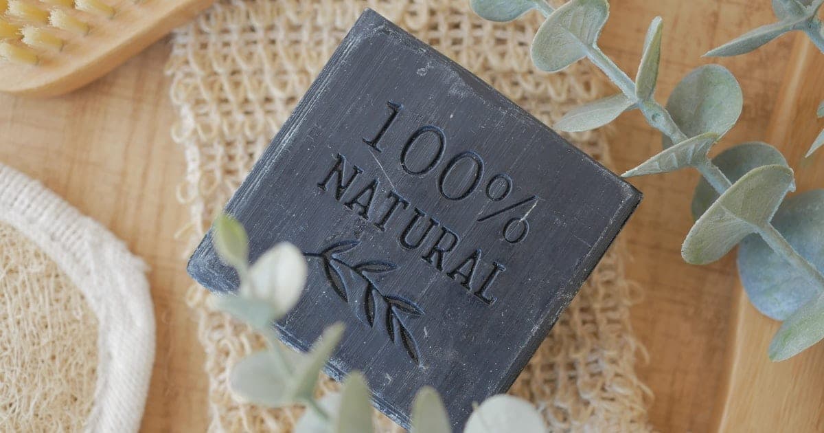 A natural soap bar embossed "100% Natural" next to a wooden brush and eucalyptus sprigs